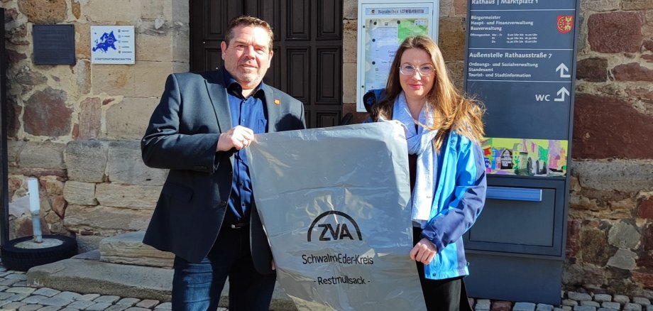 Bürgermeiser Rehm und Mitarbeiterin Frau Evtin halten einen Müllbeutel vor dem Rathaus